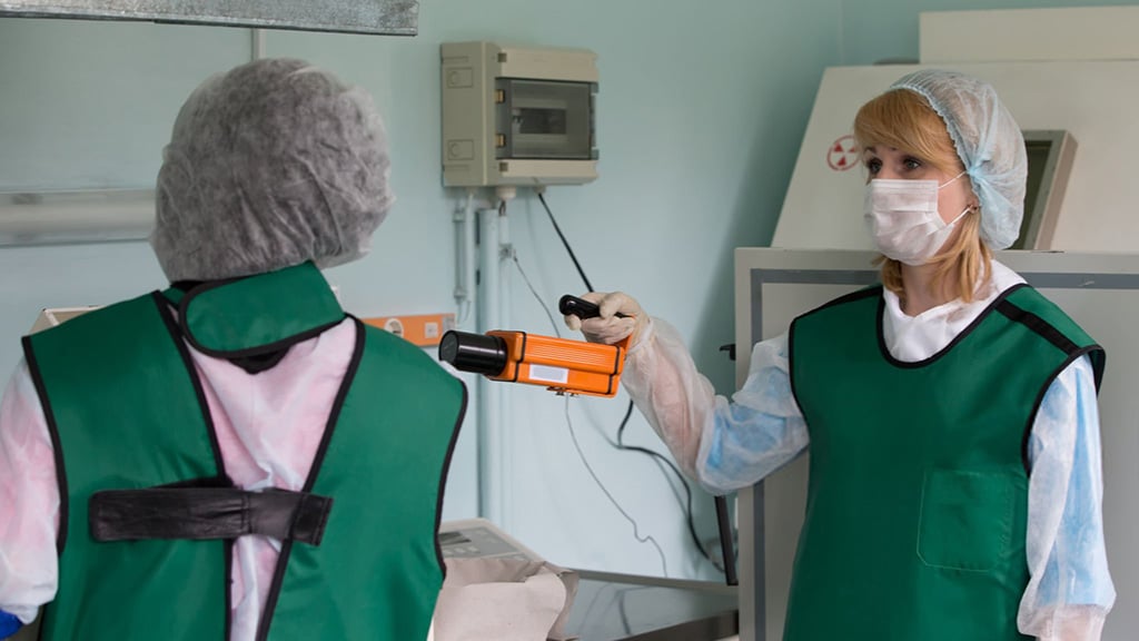Medical staff in protective gear using a radiation detector.